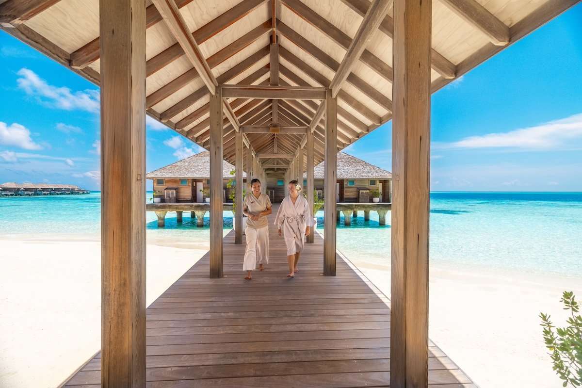 Guests in bathrobes walking the resort jetty toward the overwater Sulha Spa