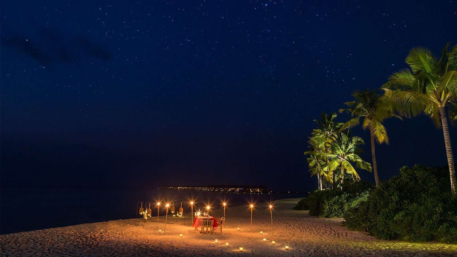 A candlelit dinner table set on the beach at night